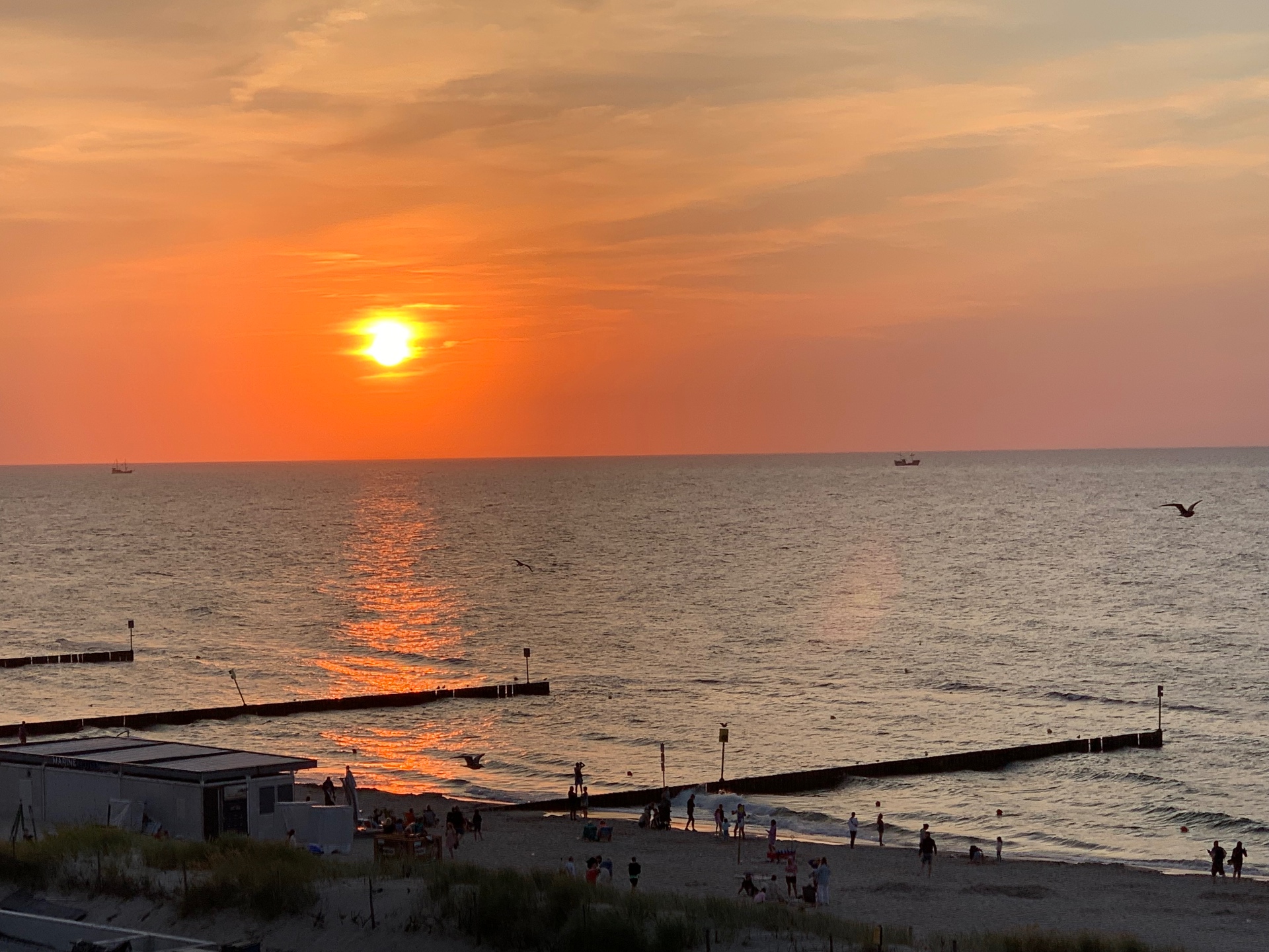 Złoty zachód słońca z nadmorskiego deptaku - sylwetki plażowiczów cieszących się ciepłym wieczorem nad morzem