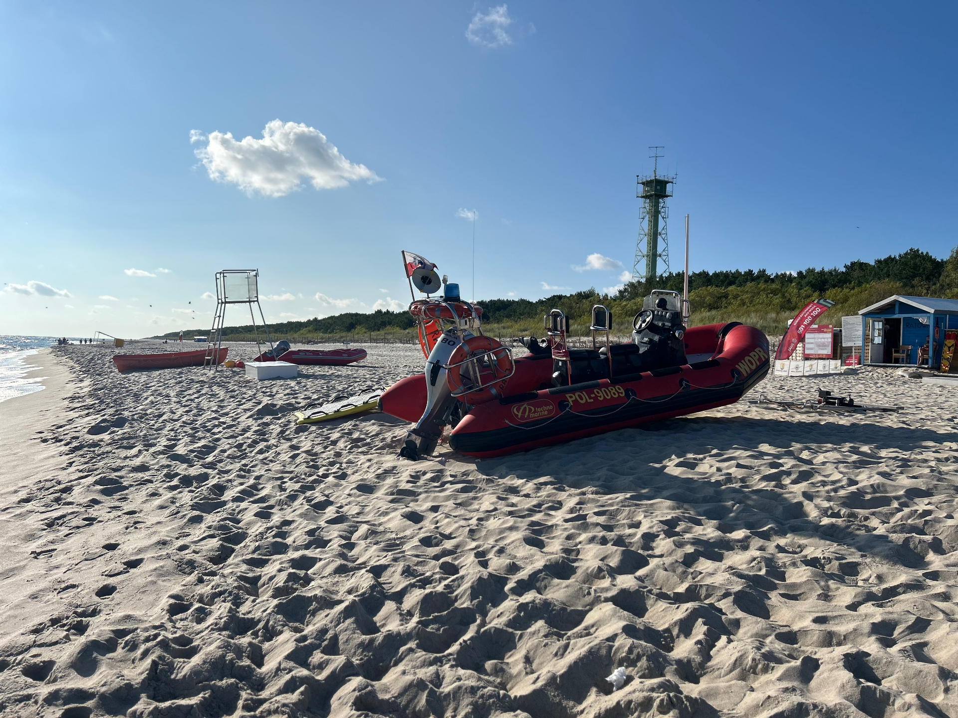Łodzie ratunkowe WOPR stacjonujące na piaszczystej plaży - gotowe do akcji, z wieżą obserwacyjną w tle
