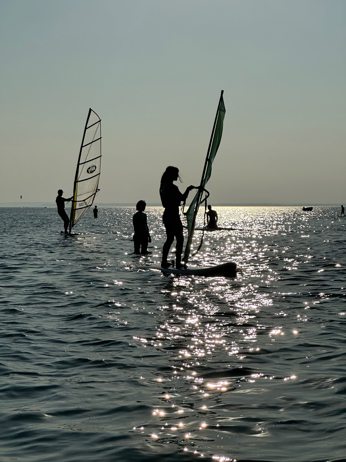 Sylwetki windsurferów o złotej godzinie - lśniąca woda odbijająca zachodzące słońce