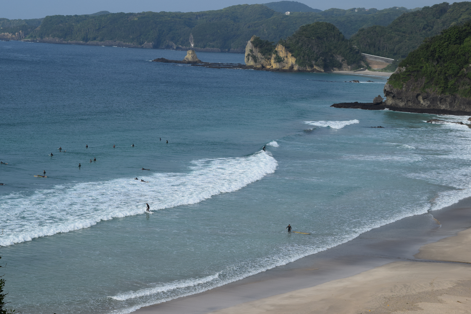 Surferzy łapiący fale na japońskiej plaży - piękna linia brzegowa z dramatycznymi klifami w tle