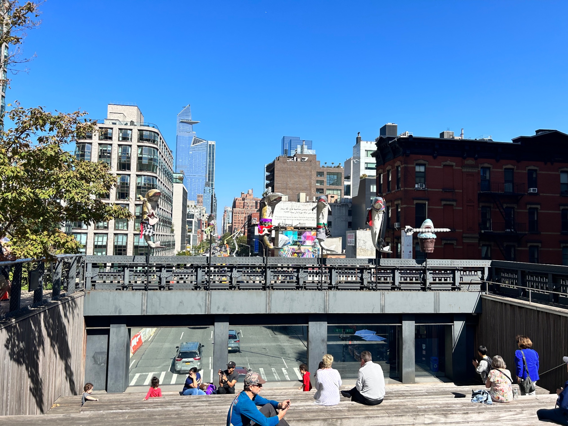 Wyniesiony park High Line - odwiedzający relaksujący się na miejskich schodach z kolorowymi rzeźbami i widokiem na Manhattan